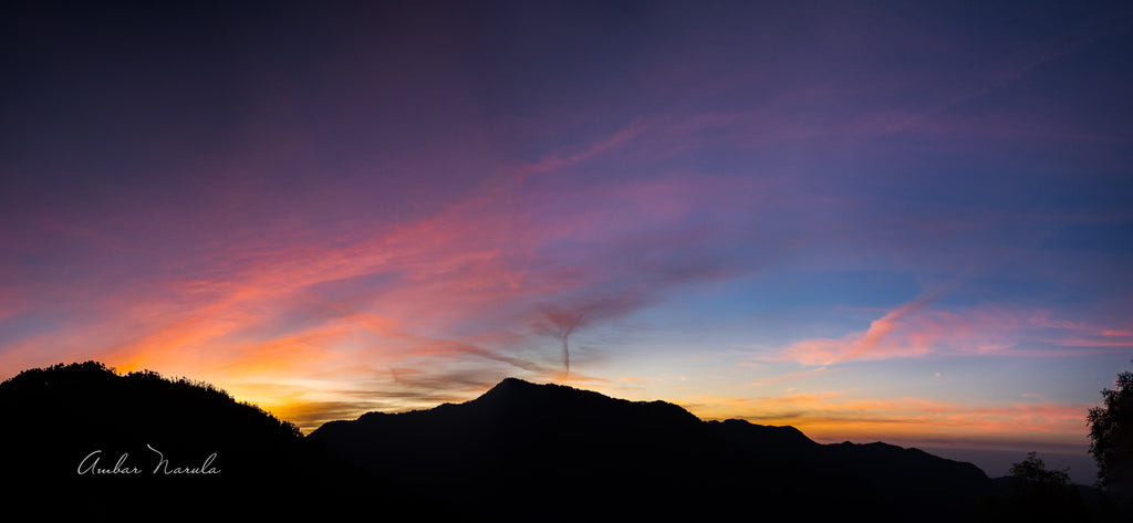 A beautiful panoramic photo of the sun setting behind a range of hills. The sky is alive with pinks, oranges and purples, cast on wispy clouds floating over the mountainous landscape. Have a beautiful day everyday, with this photo hanging on your wall! Prints available now!