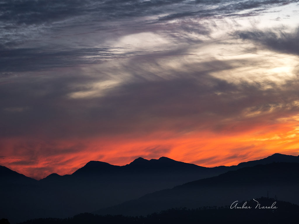 A spectacular photo of a sunset in the mountains. The sun is disappearing behind the peaks but the sky is painted in vivid oranges and yellows which makes the sky look like its on fire. Prints available.