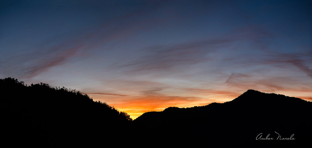 A beautiful panoramic photo of the sun setting behind a range of hills. The sky is alive with pinks, oranges and purples, cast on wispy clouds floating over the mountainous landscape. Have a beautiful day everyday, with this photo hanging on your wall! Prints available now!