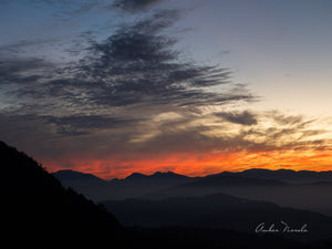 A spectacular photo of a sunset in the mountains. The sun is disappearing behind the peaks but the sky is painted in vivid oranges and yellows which makes the sky look like its on fire. Prints available.