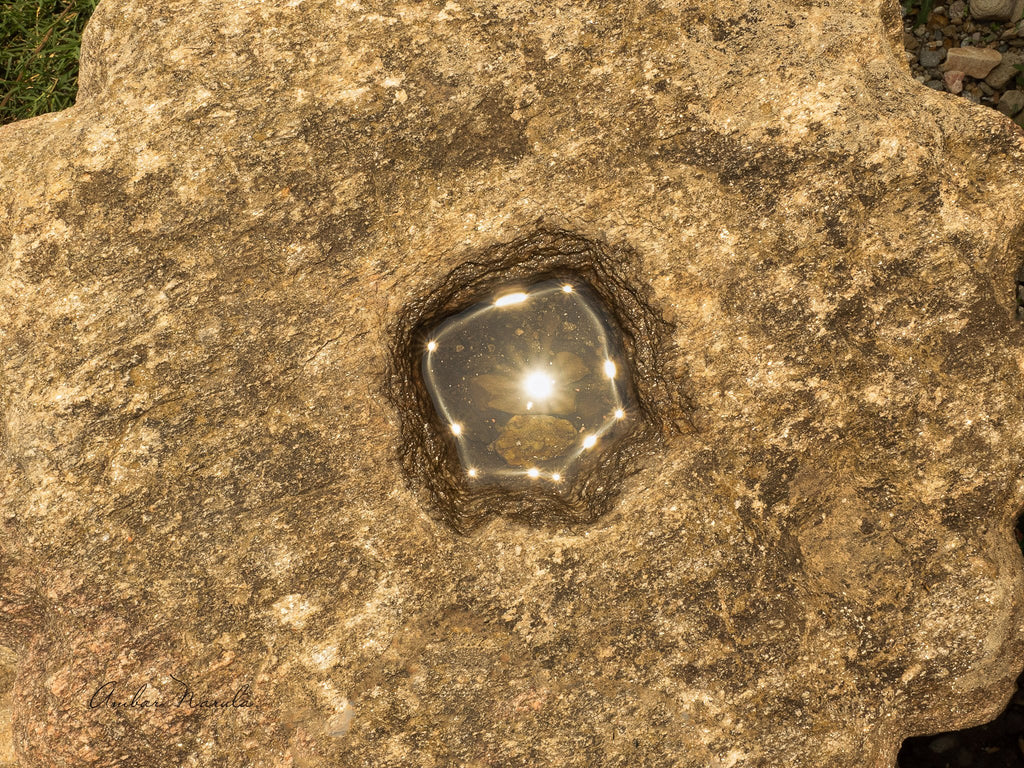 A bright sun overhead creates some lovely sunbursts in a little pool of water collected within a stone that's fallen off the top of a Sun Temple in northern India.